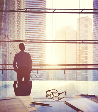 silhouette of business man standing in front of large city office window